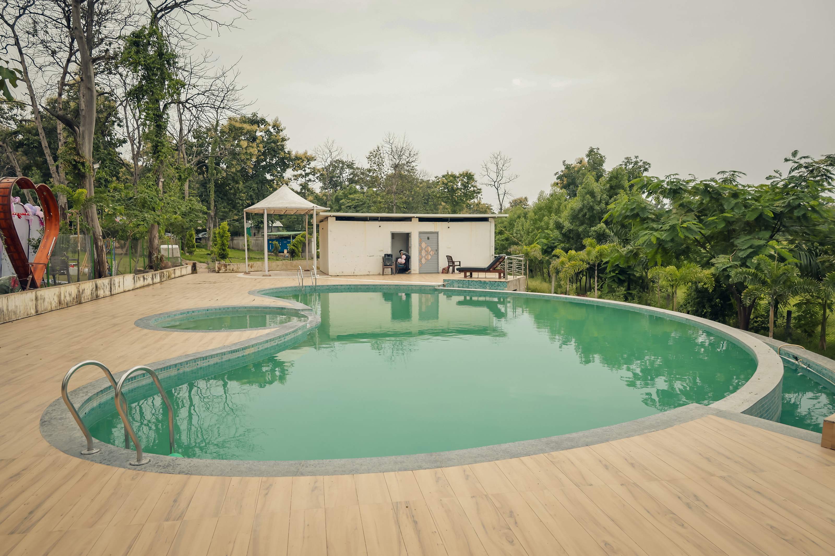 Swimming pool with wooden deck and changing rooms, surrounded by trees